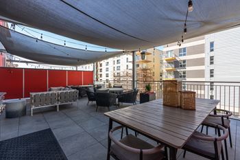 A wooden table with chairs is set up on a patio with a red wall in the background.